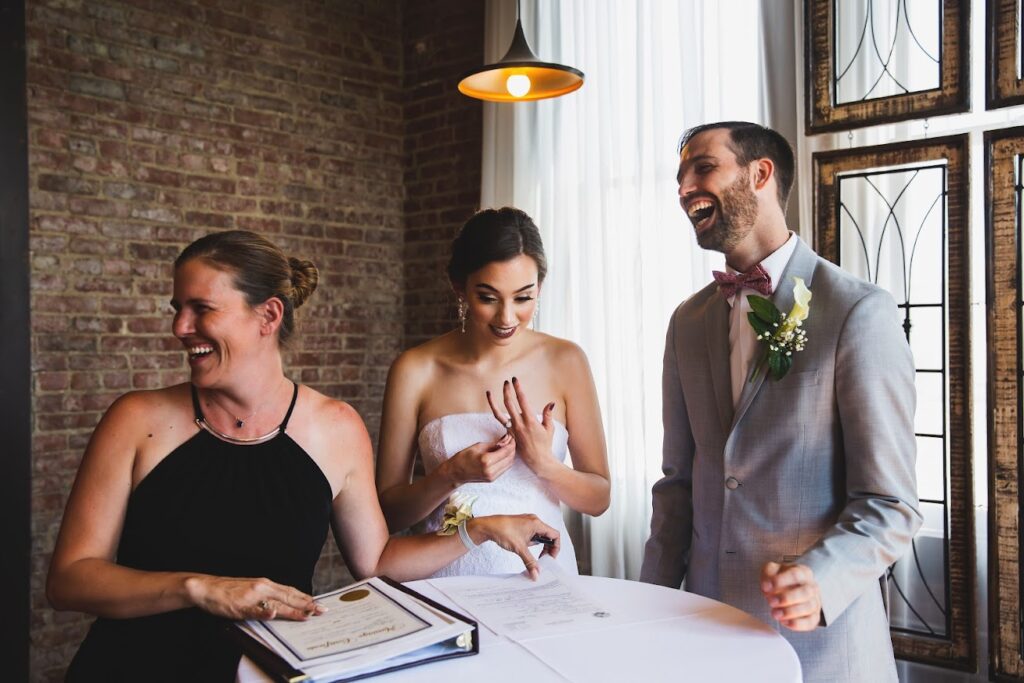 A bride and groom standing at a table with their wedding officiant